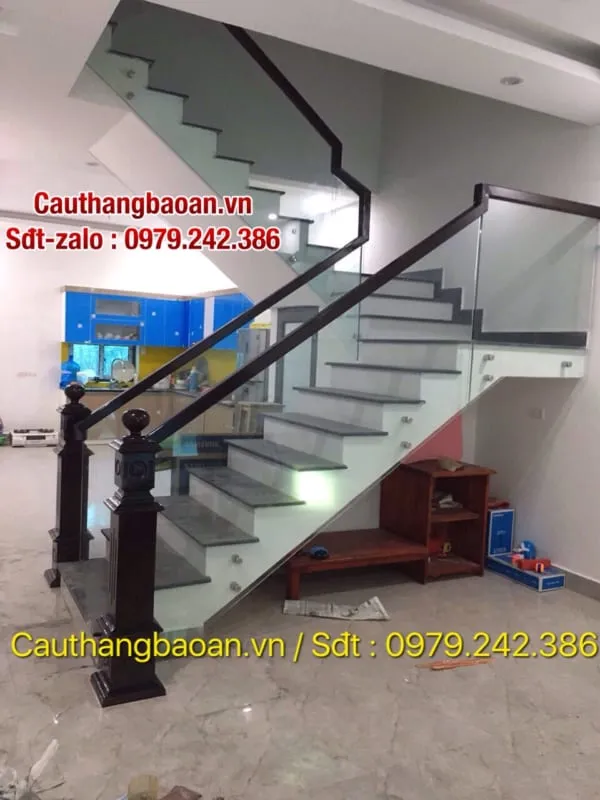 Cầu thang kính cường lực tay vịn gỗ tạo không gian thoáng đãng, gầm cầu thang tận dụng làm kệ